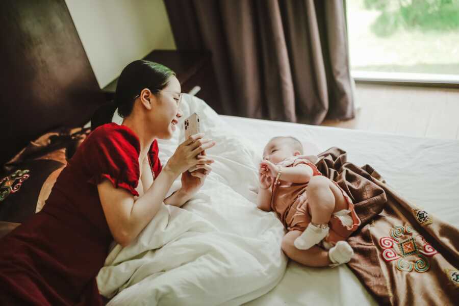 mom on the bed with her baby showing her something on her phone