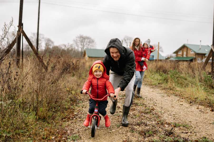 man outside with his family teaching his son to bike