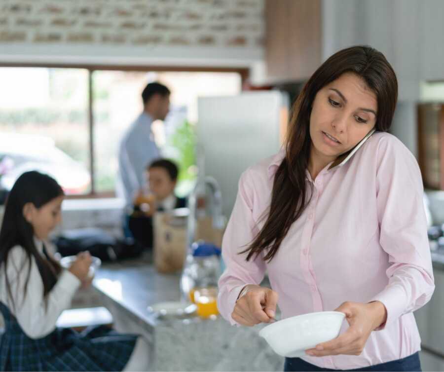 Mom prepares food while talking on the phone with family in the background of the kitchen.