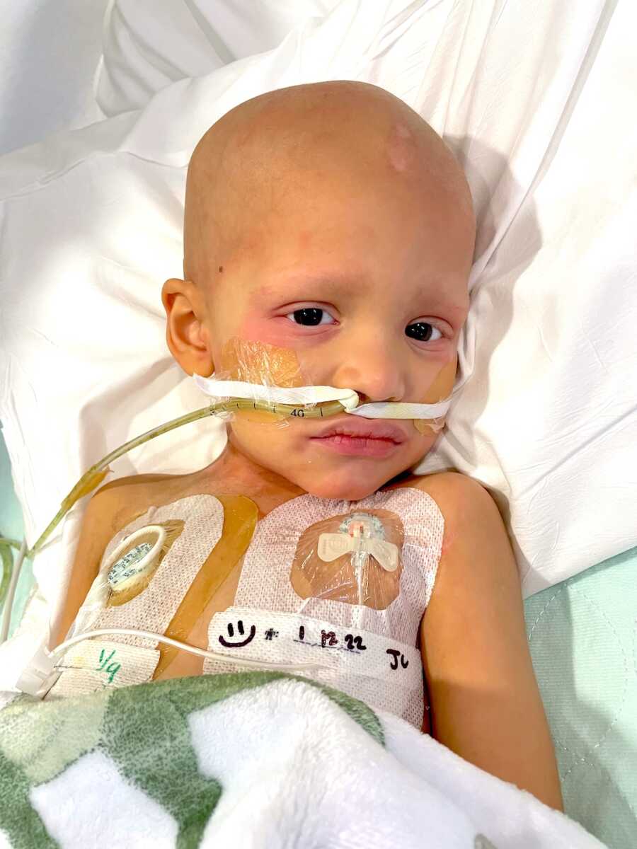 boy with childhood cancer sits lays in bed for his treatments