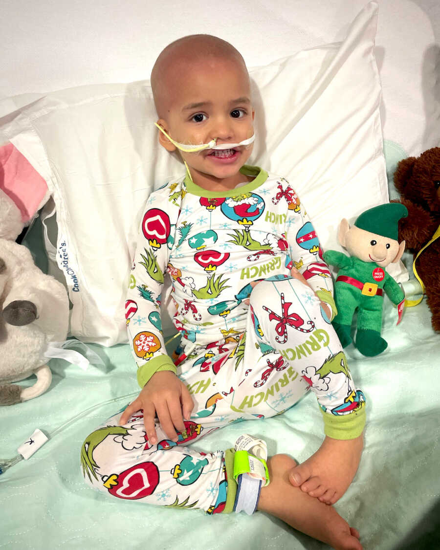 boy with childhood cancer sits in Christmas pajamas while getting treatments