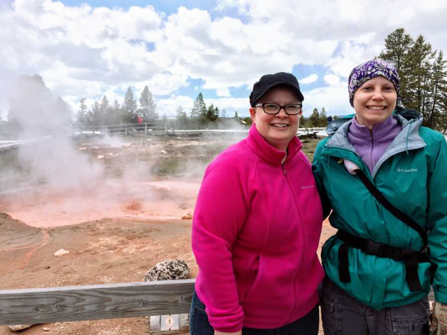 A couple stands by a geyser wearing pink and green jackets