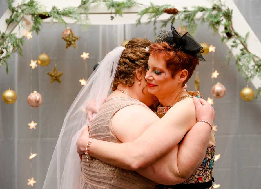 Brides hug after kissing at the altar during their wedding