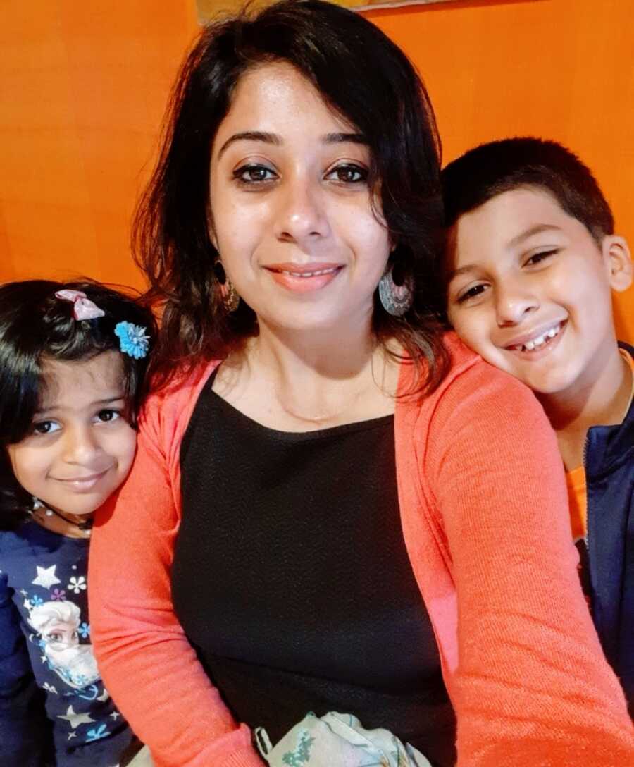 A mom with her daughter and son leaning against an orange wall