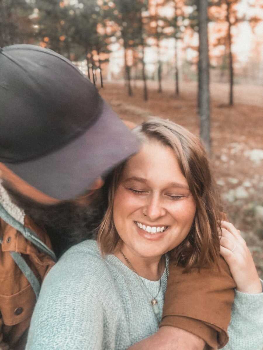 Husband wearing baseball cap puts arm around wife smiling back.