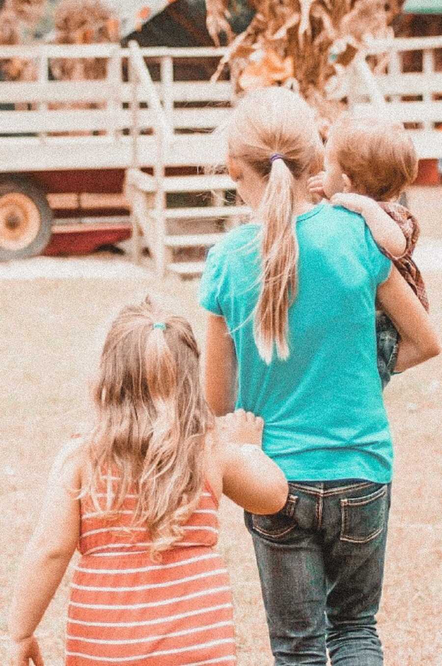 Adopted birth daughter holds little half sister with other sister trailing behind. 