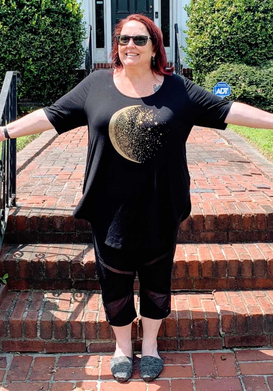 An overweight woman stands by brick steps with her arms outstretched