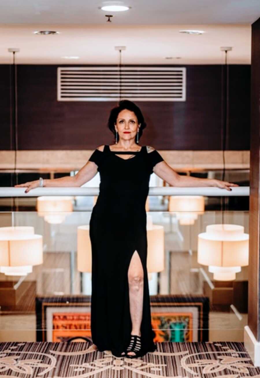 A woman wearing a black dress stands against a glass railing