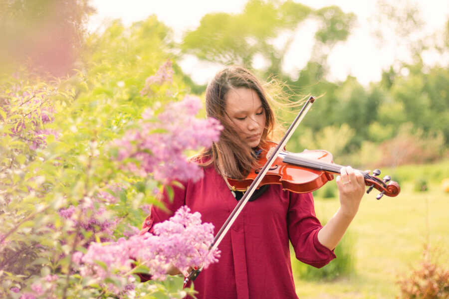 adoptee plays her violin amongst flowers and greenery