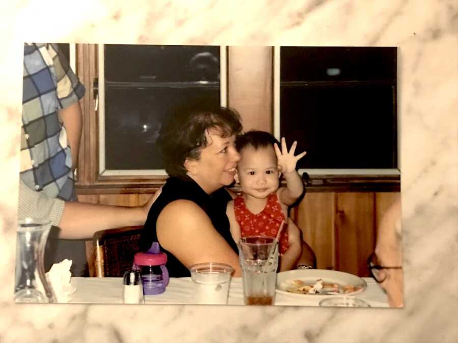 adoptee sits in her adoptive mother's lap and waves to the camera