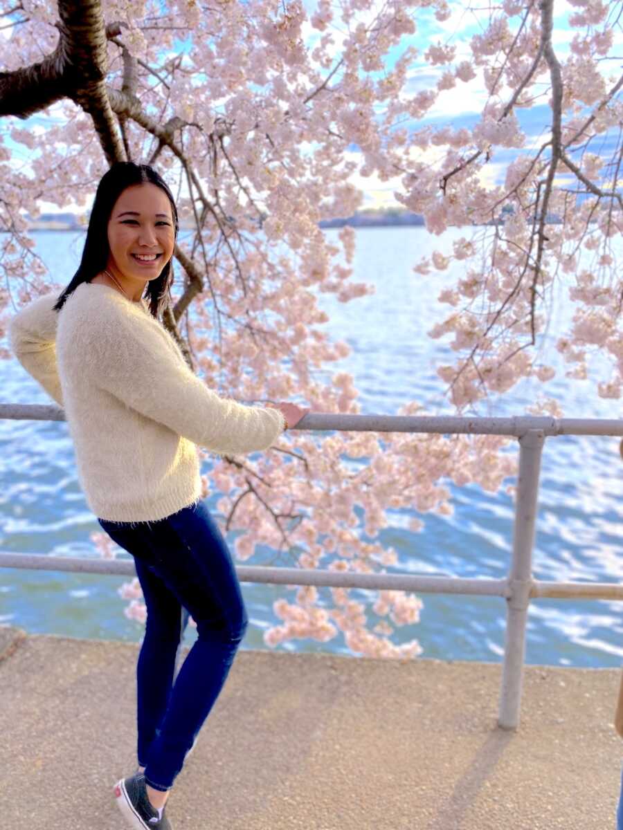 adoptee stands in front of cherry blossoms and the water