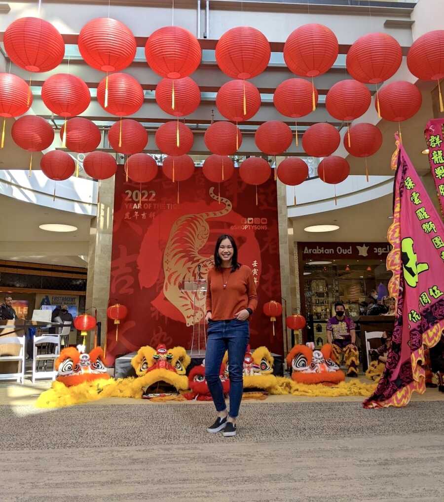 Chinese adoptee stands in front of a Chinese New Year display