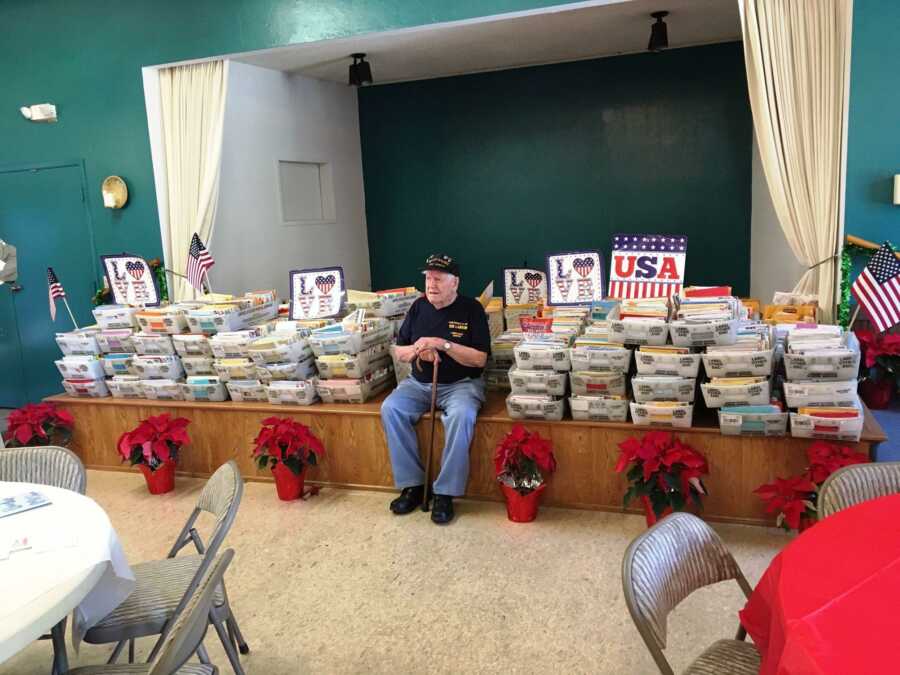 WWII vet sits in front of hundreds of bins full of birthday cards. 