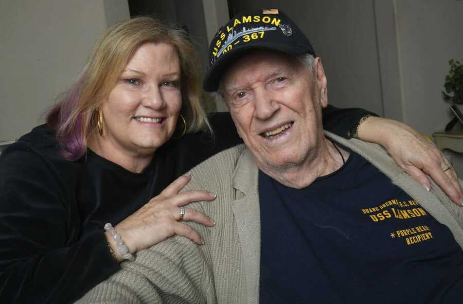 Daughter has arms around father wearing U.S. Navy shirt and baseball cap. 