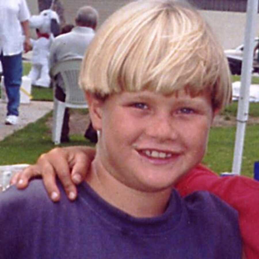 Blonde boy wearing blue t-shirt smiles at camera. 