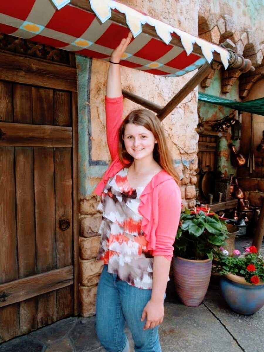 A young woman stands outside wearing a pink cardigan and blouse