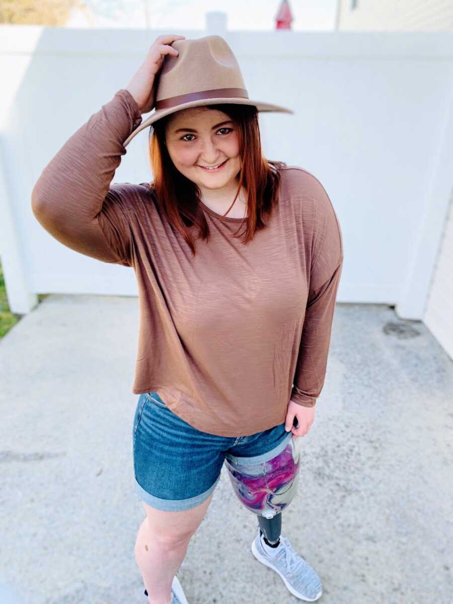 An amputee stands on her new prosthetic leg wearing a hat