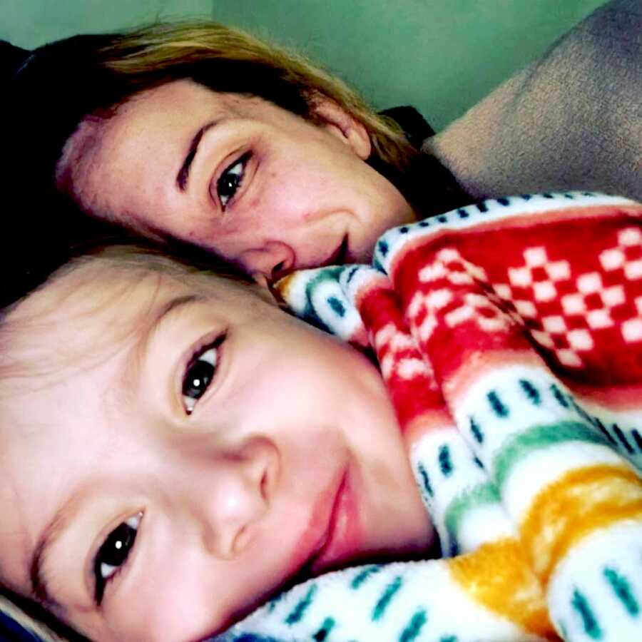 mother snuggles up in bed with her daughter and a blanket