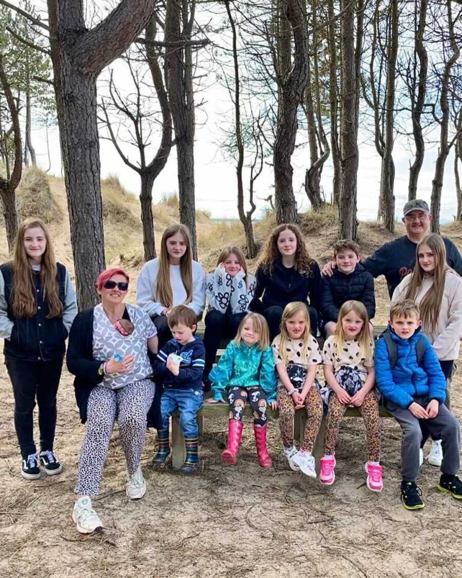 12 children and mom and dad sitting on bench in woods, smiling for photo