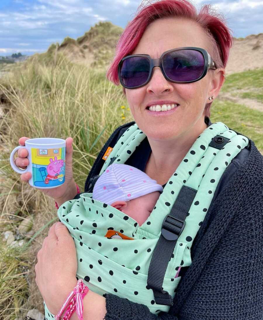 mom walking with baby on chest with a cup of coffee in hand