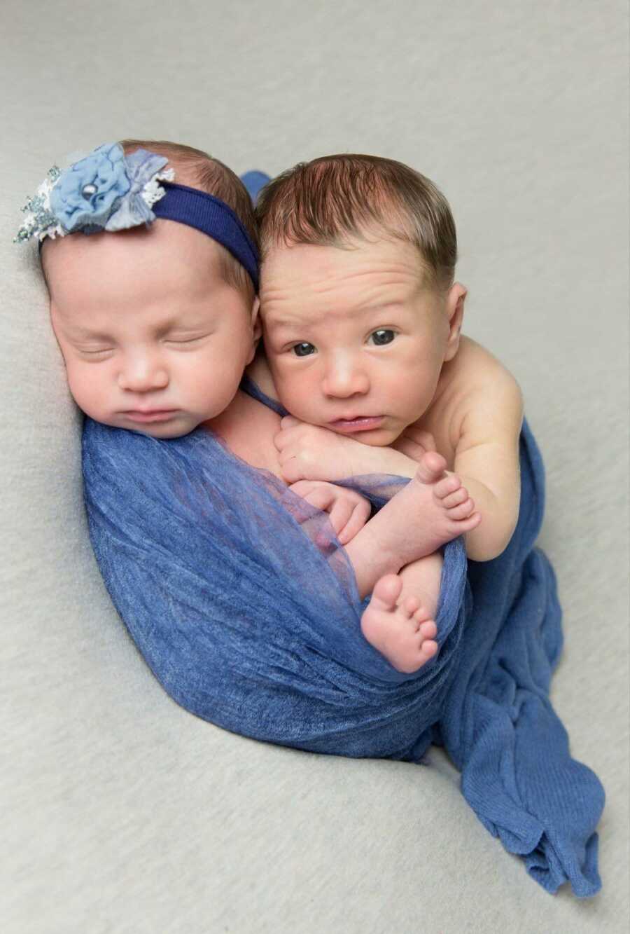 Newborn twin babies curled up next to each other in a light blue blanket