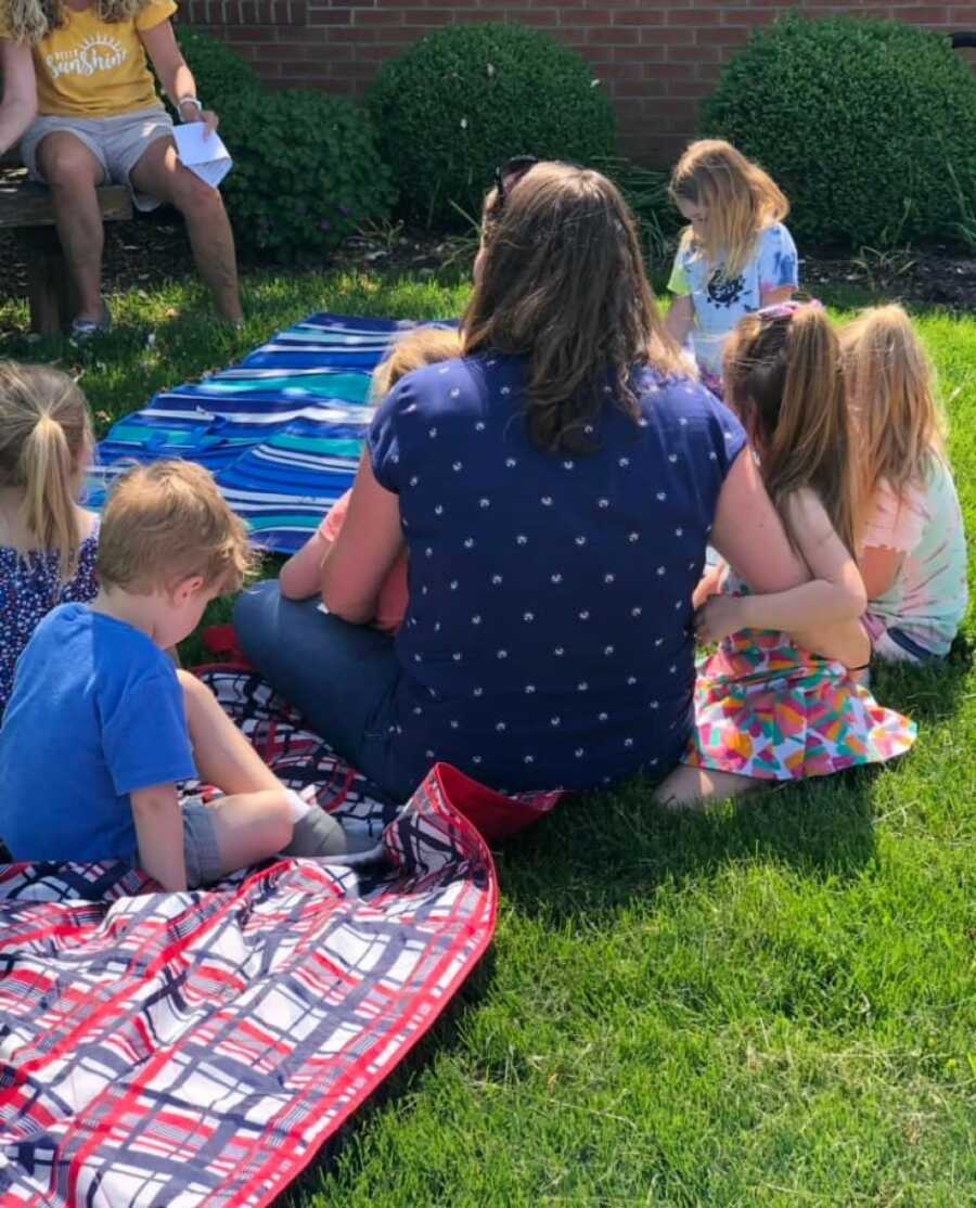 preschool teacher sitting with her students on the grass