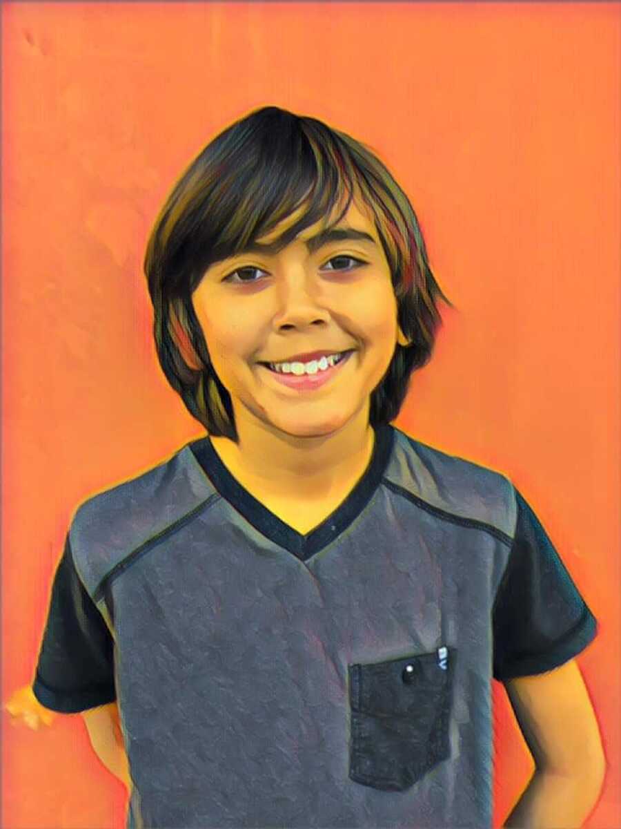 A young boy wearing a black T-shirt stands against an orange background