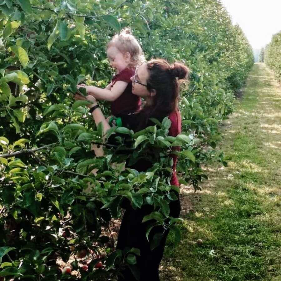 Mom lifts daughter up to pick fruit off a vine during a walk