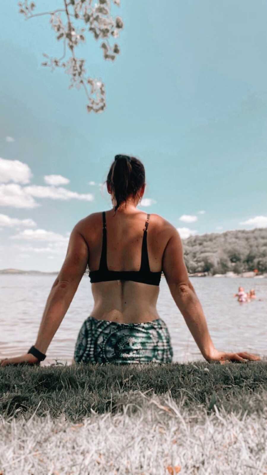 Mom of four looks out over the water while sitting on a log in a bikini