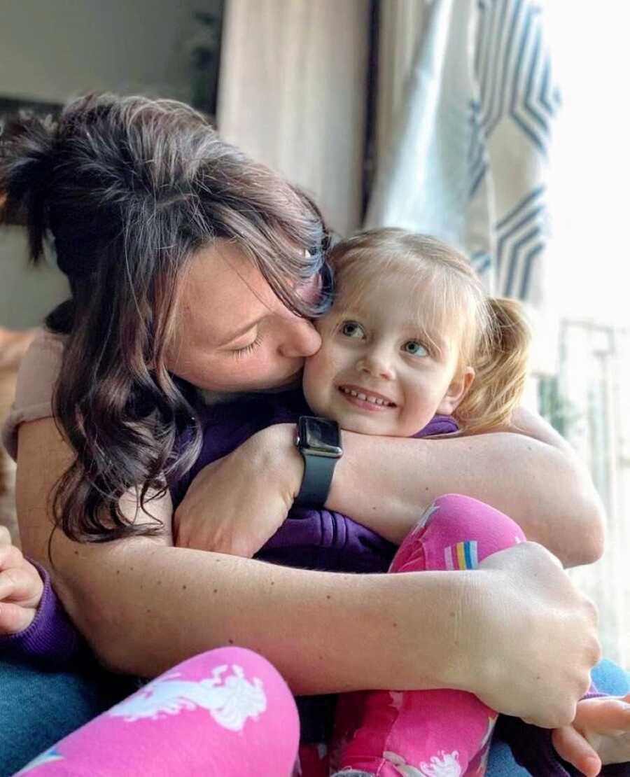 Mom snuggles with her daughter and kisses her cheek