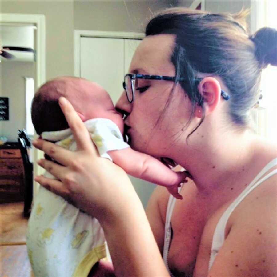 mom holding her first born daughter and giving her a kiss on the face 