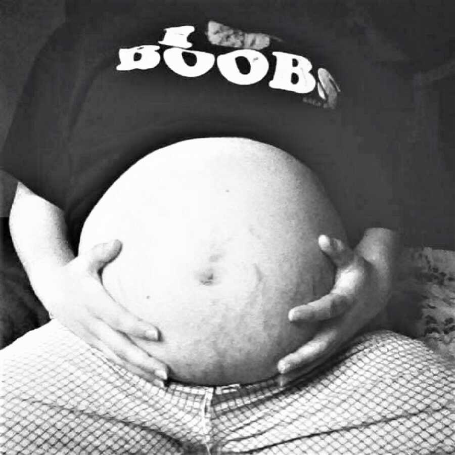 closeup of bare pregnant belly with stretch marks and hand around it in black and white 