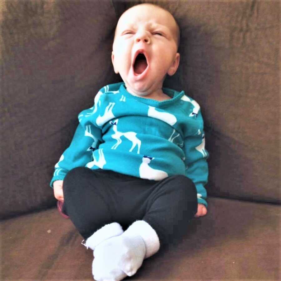 newborn baby girl sitting on a brown couch and yawning