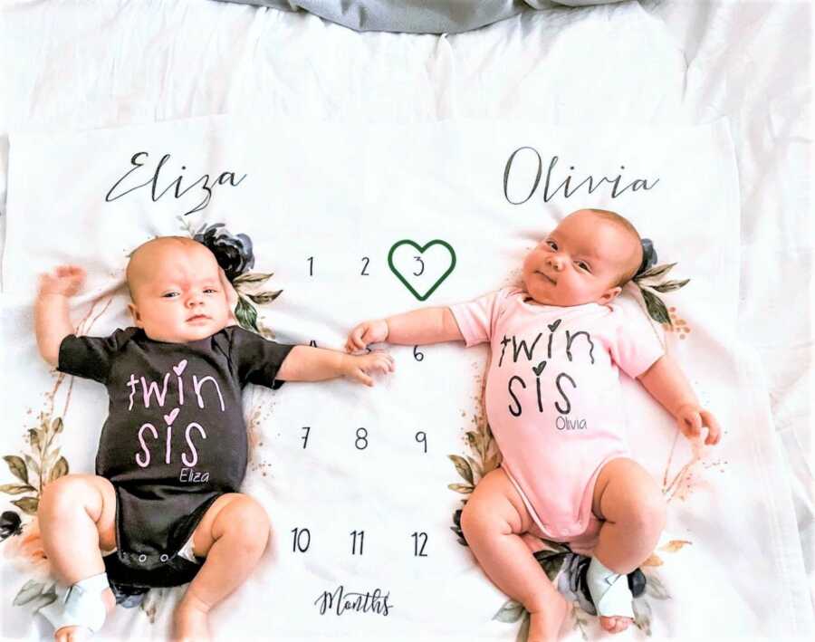 newborn twins wearing onesies with words "TWIN SIS" 