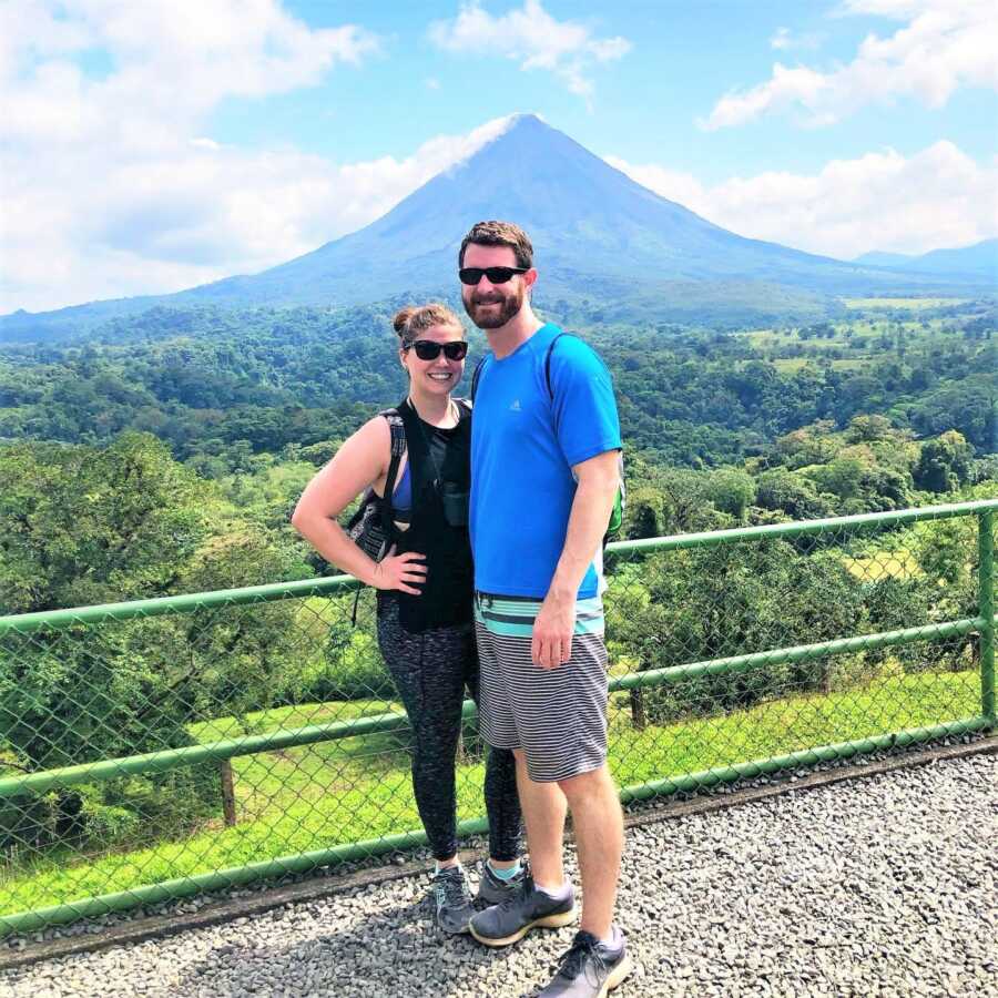 Couple who are traveling standing next to each other with tall mountains and trees in the back