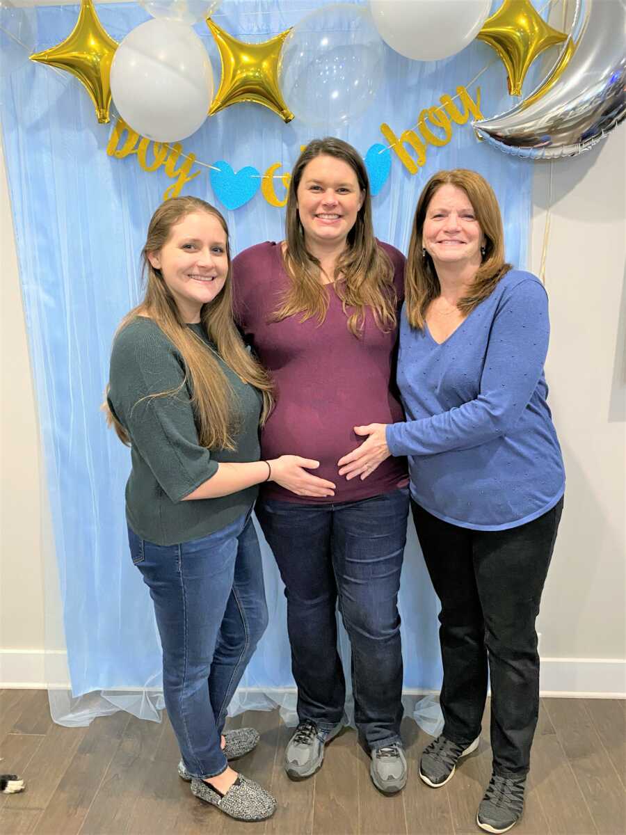 pregnant woman at her baby shower for her baby boy with her mom and sister holing her pregnant belly 