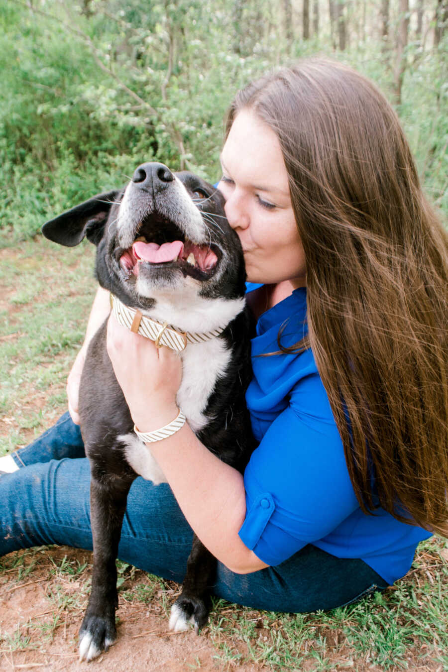 a woman sitting on the grass giving her black and white dog a kiss on the cheek 