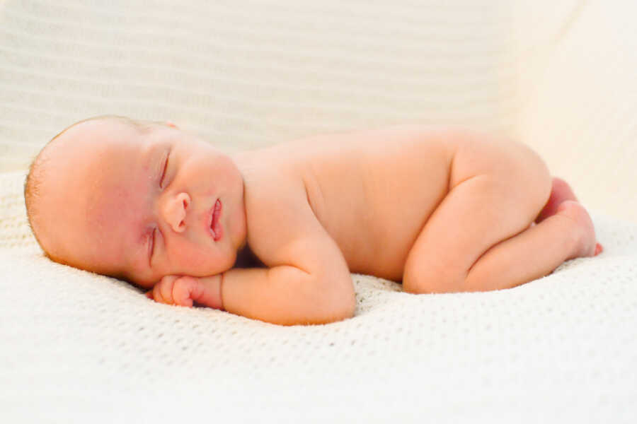 naked baby boy sleeping on his stomach with his head resting on his hands 