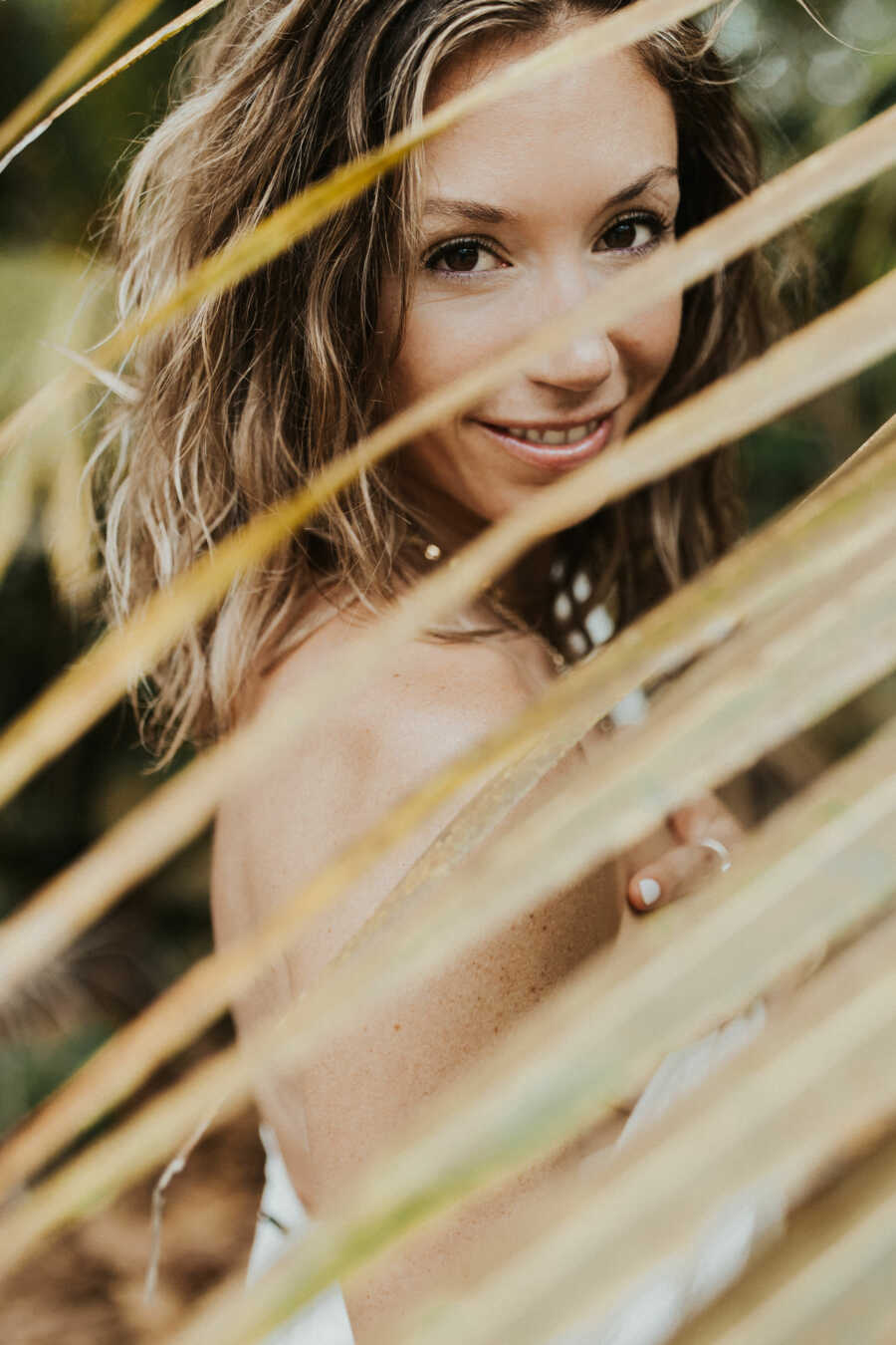 woman in a white dress photographed though a palm tree branch