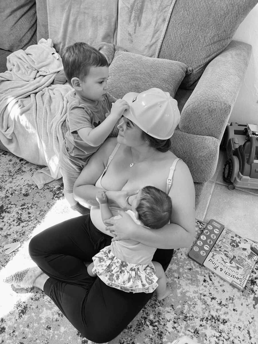 Woman breastfeeds her baby while her toddler attempts to steal her hat