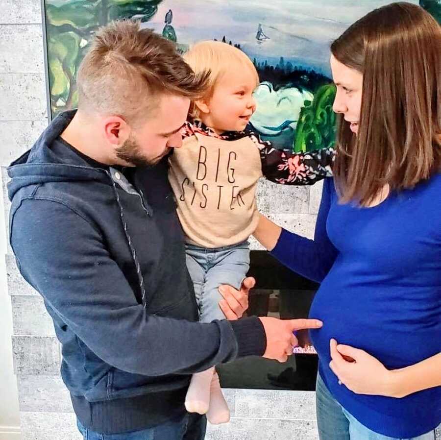 Daughter wears "big sister" shirt while pointing to mom's pregnant belly