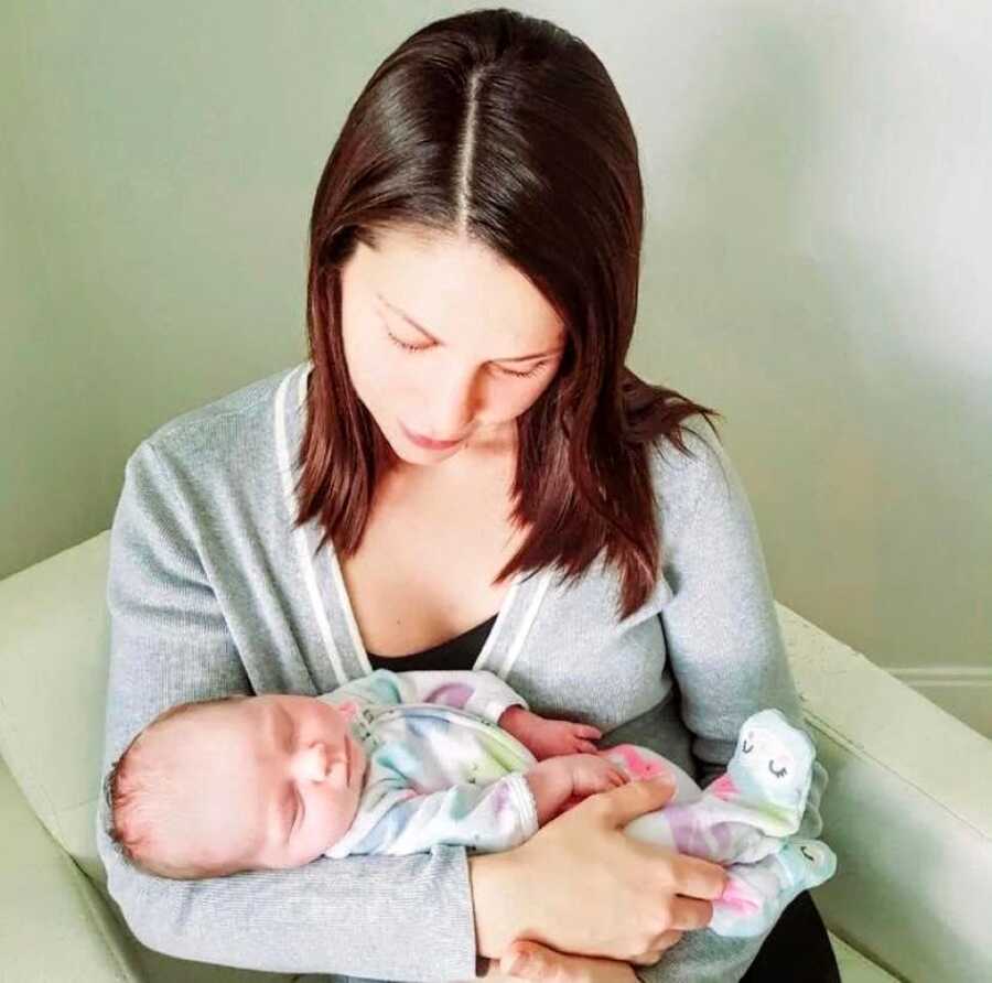 Mom looks down at newborn daughter sleeping in her arms