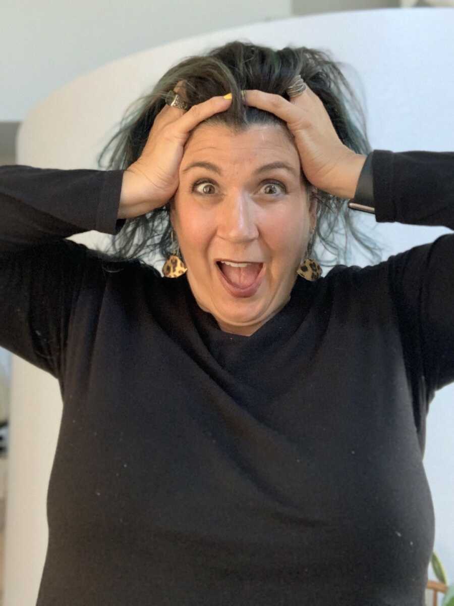 A woman holds both sides of her head and makes a surprised face
