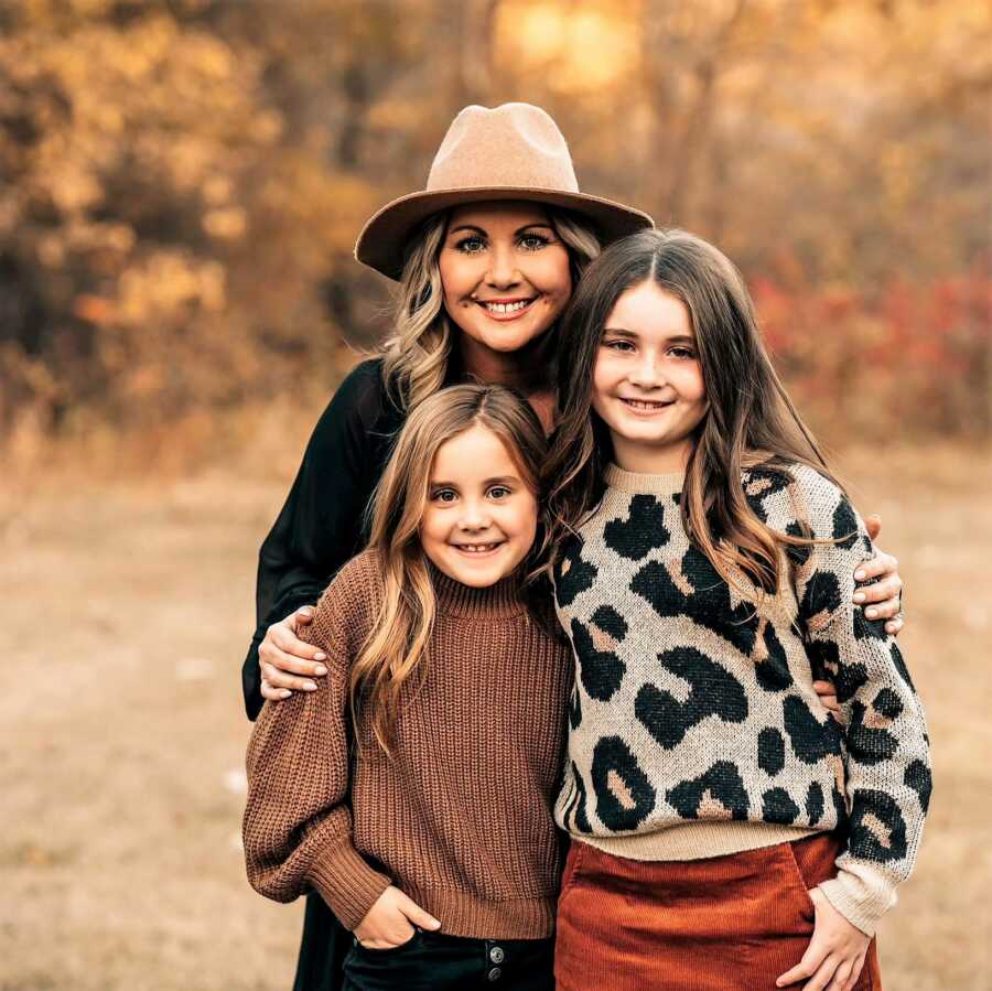 fall colored portrait of mom and her two daughters outdoors wearing earth-tone outfits 