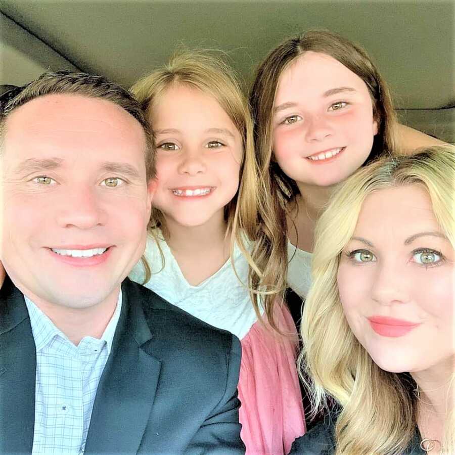 selfie of mom, dad and two daughter sitting inside of a car smiling