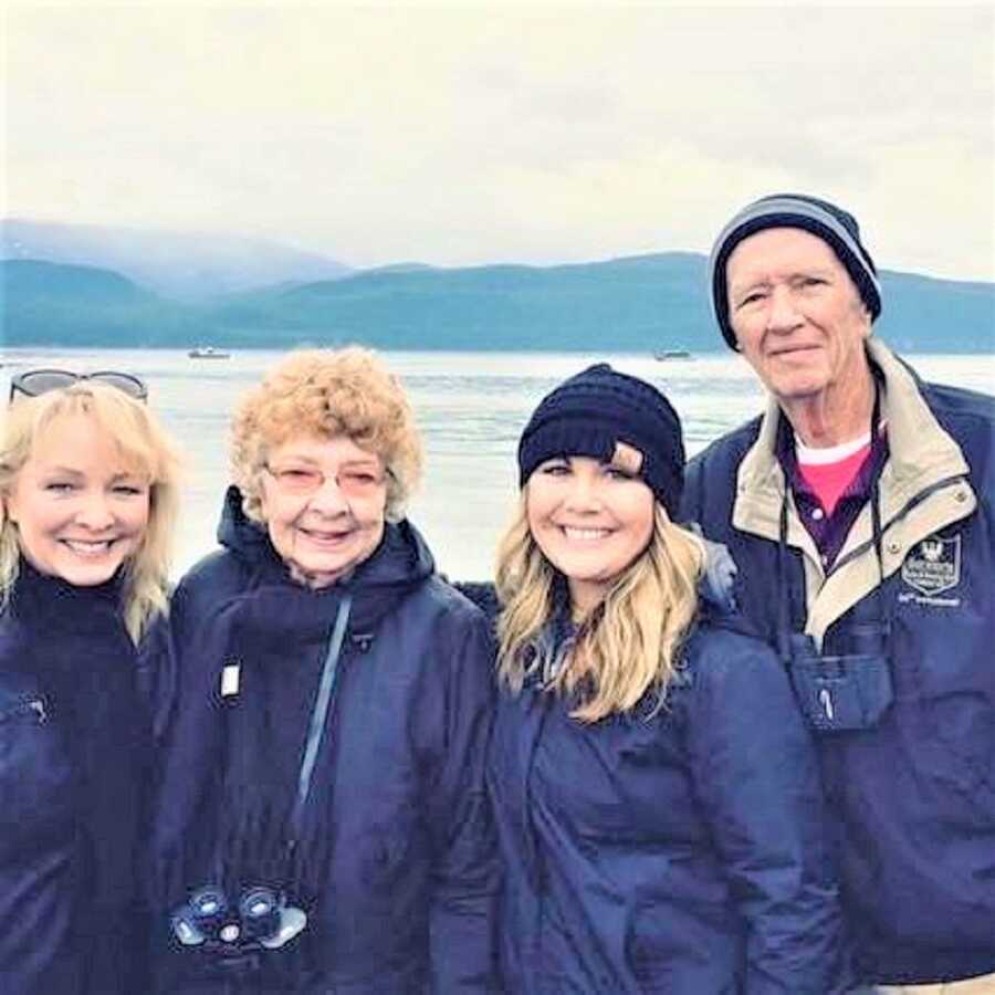 three generations of women in a family and a grandpa standing in front of a lake with mountains in the background 