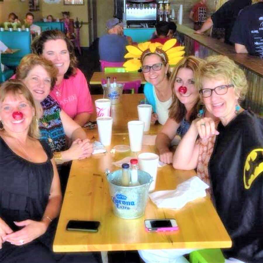 different generations of a family of women having drinks at a restaurant while wearing props such as red noses and a sunflower hat