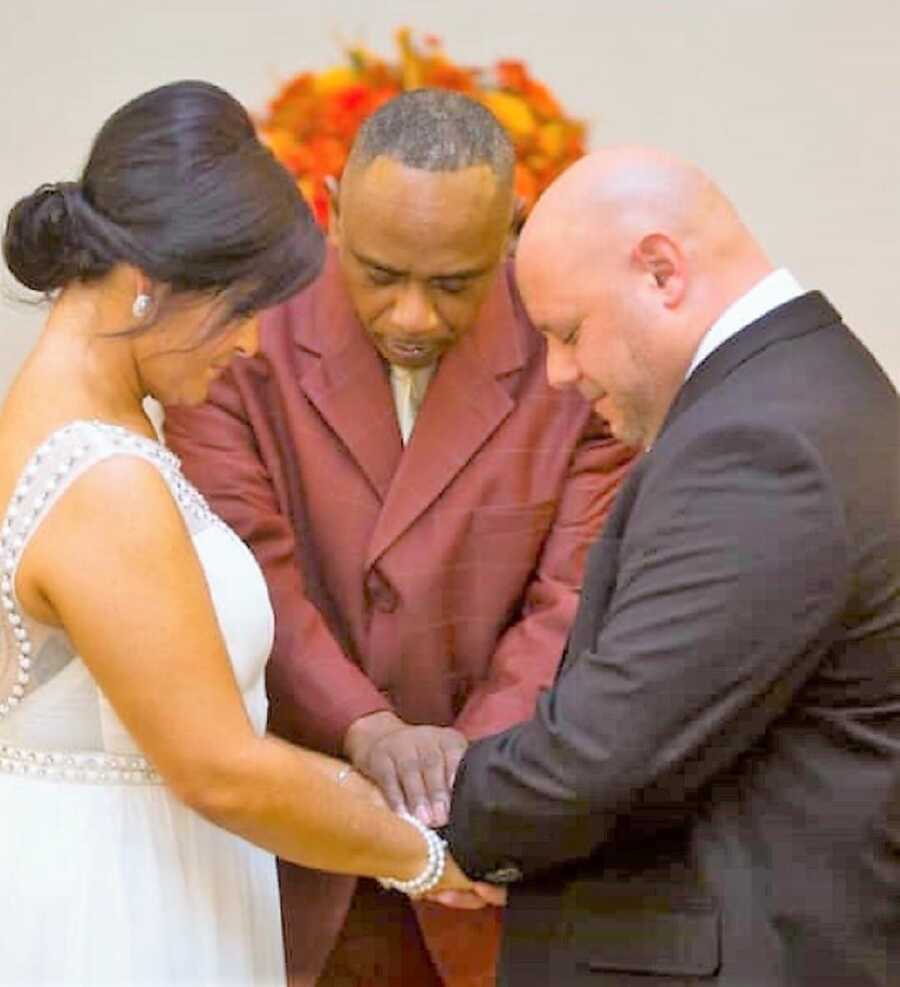 husband and wife during their wedding ceremony standing in front of each other holding hands with their eyes closed