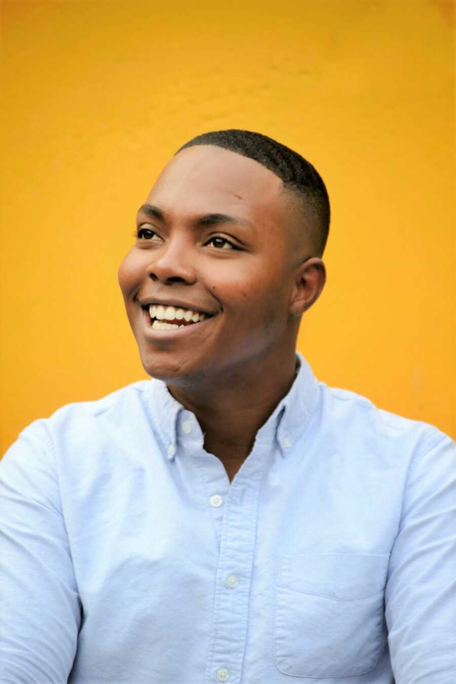 Portrait of black man with yellow background smiling with his head tilted to the right 