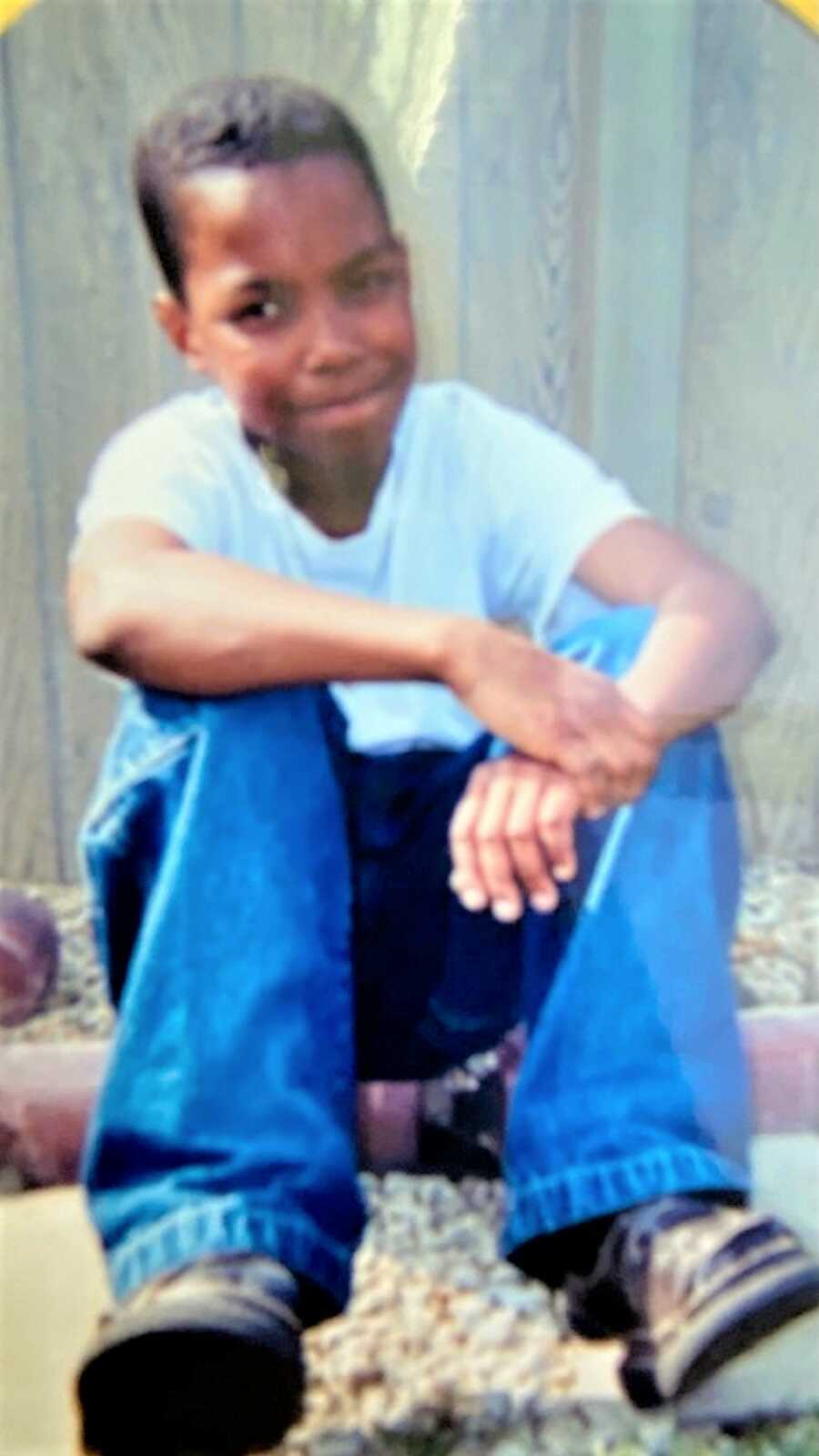 Young black boy sitting on the street wearing white shirt and jeans 